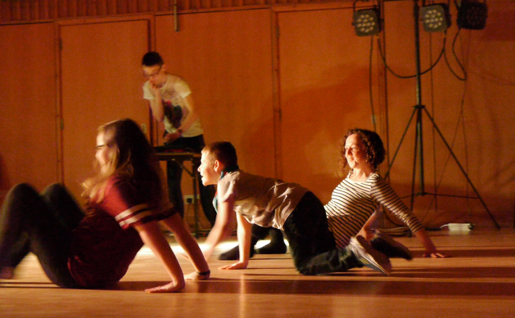 Julia and two young people moving low across the floor with a young DJ in the background