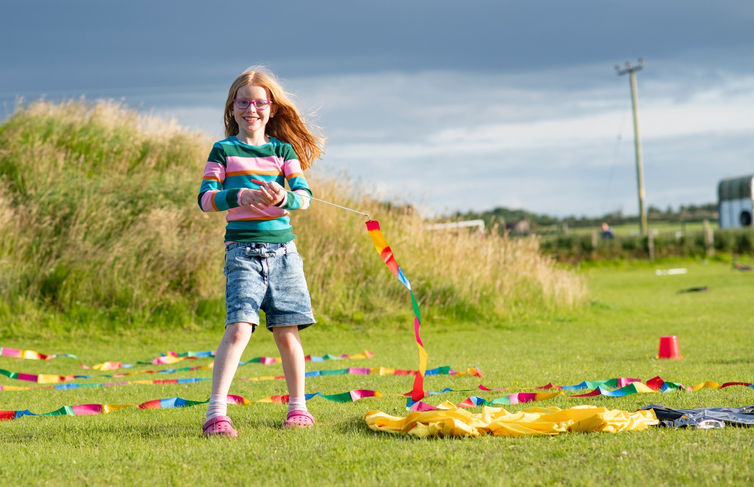 A young girl standing in a park holding a brightly coloured ribbon